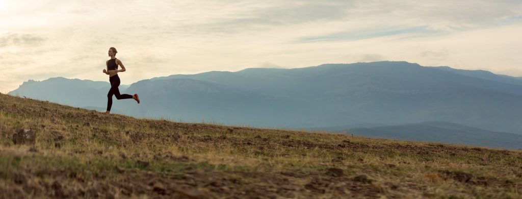 Female runner in open field with mountains in the background